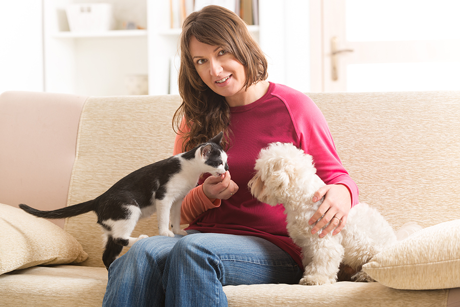 A photo of a young woman on a couch with a dog and cat.