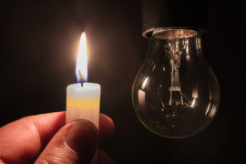 Burning candle near a switched off light bulb. Blackout, electri