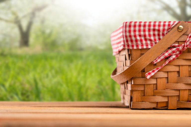 Picnic basket on a wooden table, against the backdrop of the landscape. Rest and picnic. Weekend or vacation. Concept of summer mood.