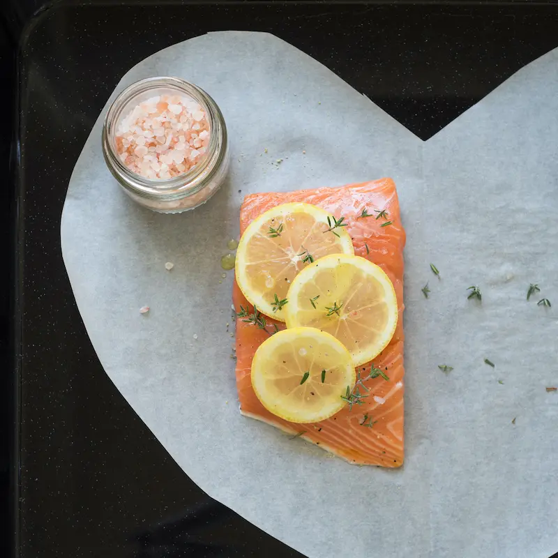 Fish in parchment paper showing salmon and lemon slices.