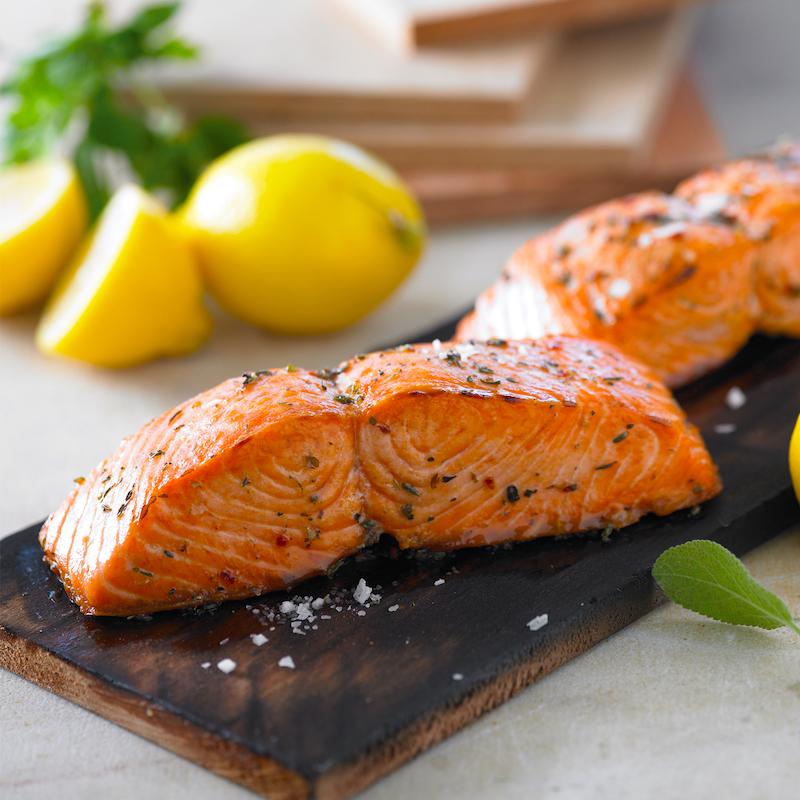 Cedar Plank Grilling showing salmon on a charred plank with lemons in background.