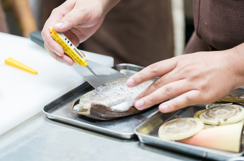 A photo of tips for cooking fish showing a person inserting a thermometer into a fillet of fish.