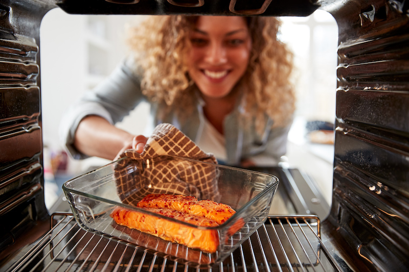 A photo of tips for cooking fish featuring a woman removing baked fish from an oven. 