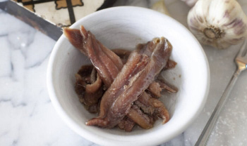 Photo of anchovy recipes featuring anchovies in white bowl. 
