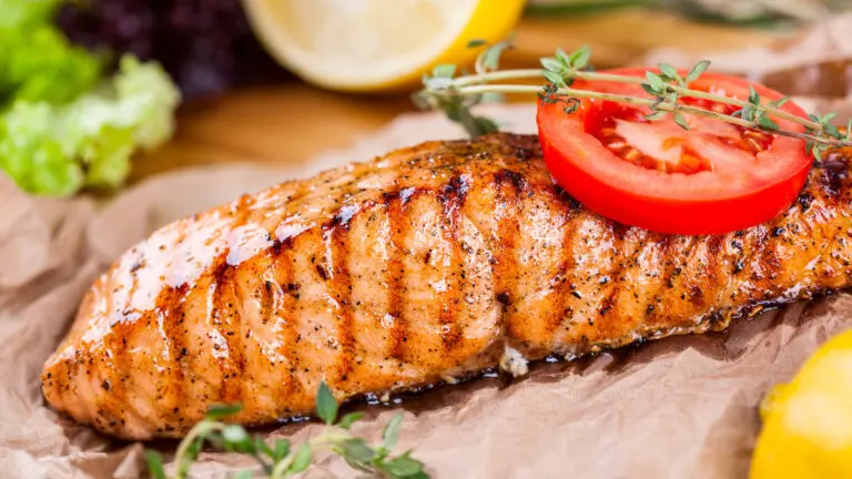 Tips for cooking fish with a slice of cooked fish on parchment paper topped with herbs and a slice of tomato.