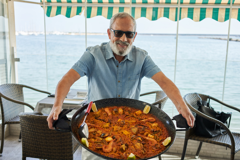 Seafood longevity: Senior grey haired man smiling confident holding seafood paella at coffee shop terrace