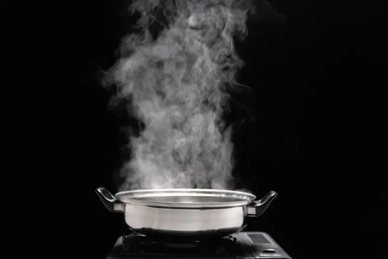 Steam over cooking pot in kitchen on dark background.