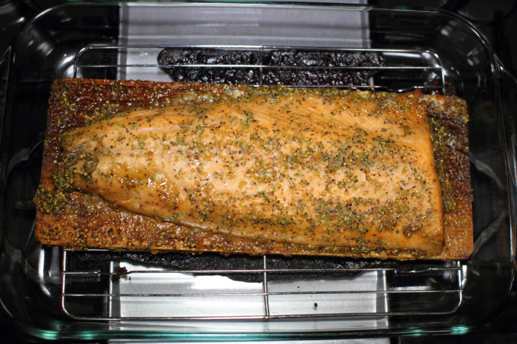 Baked cedar plank salmon on a glass baking tray resting on the stove top.