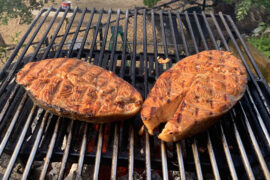 Grilled salmon steaks on a large grill outside.