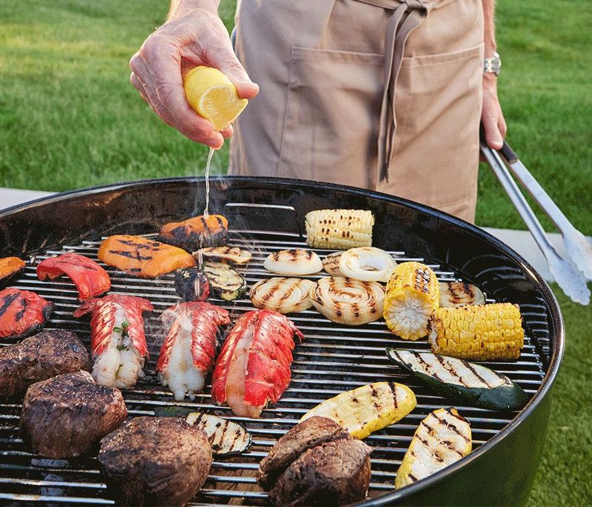 How to grill lobster with a hand squeezing a lemon over lobster tails and other items on a grill.
