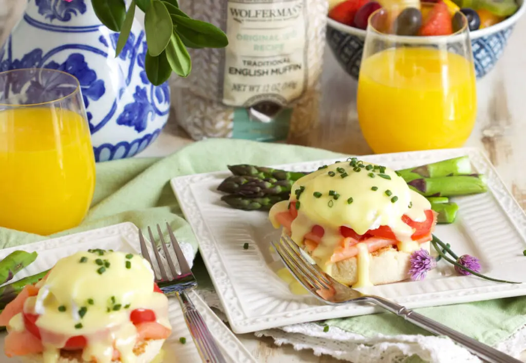 Smoked salmon eggs Benedict on two plates with two glasses of fruit juice.