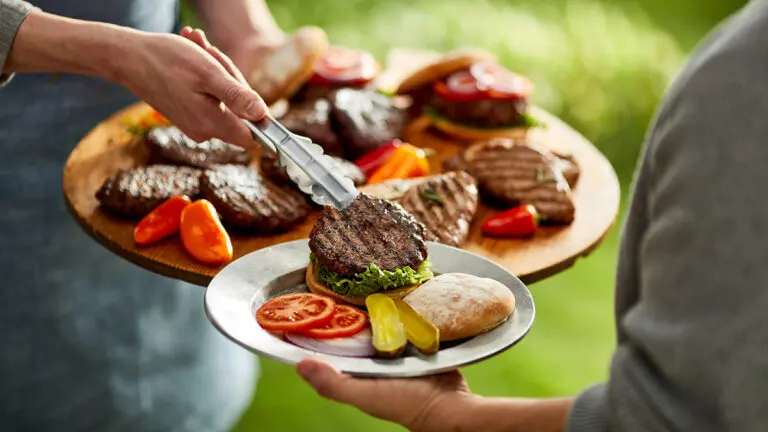 Hamburgers on a platter with a hand putting a hamburger on someone's plate.