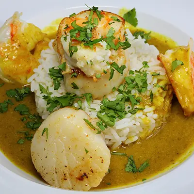 Seafood recipes with curried scallops and shrimp in a bowl of rice and broth.