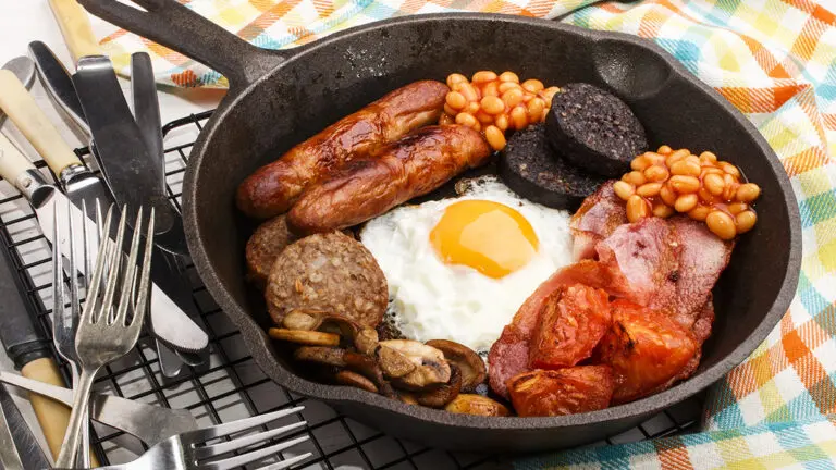 Breakfast meat in a cast iron pan with eggs and beans.