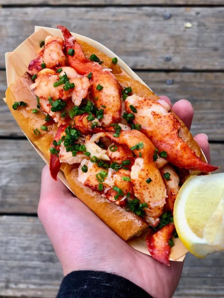 A man holding a lobster roll in his left hand.
