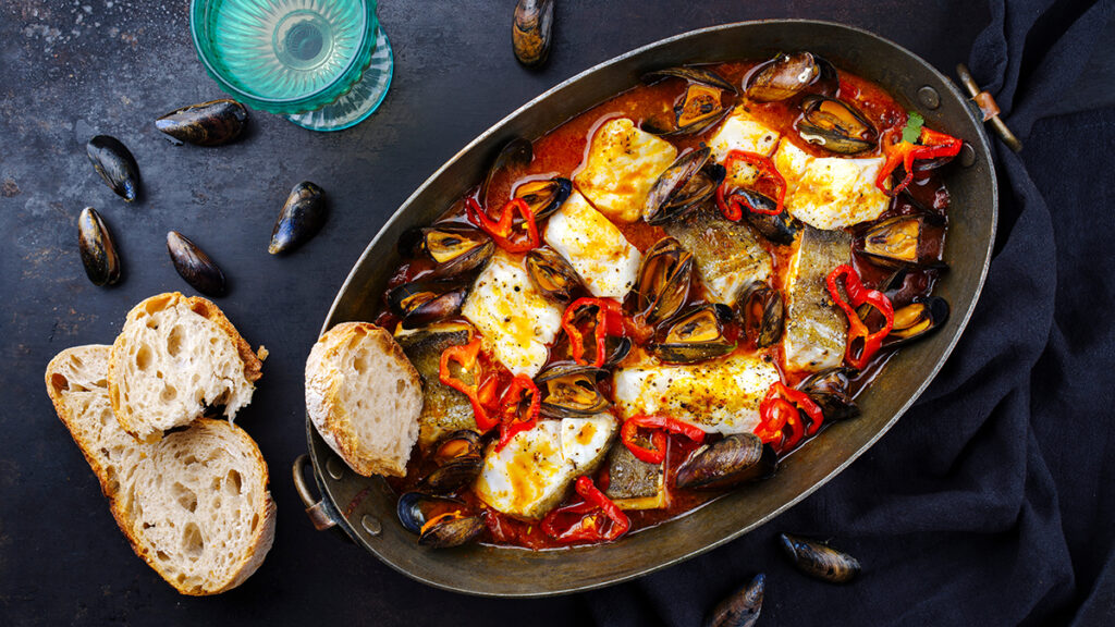 Sea bass bouillabaisse in a oval pot with crusty bread.