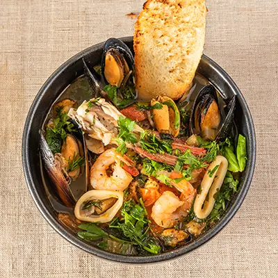 Homemade cioppino in a bowl and toast, top view Italian American seafood soup fish, mussels, shrimp and squid.