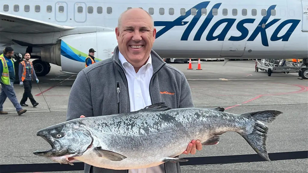 Vital Choice co-founder holding a salmon with an airplane in the background.