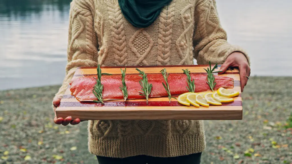 Featured catch with a person holding a salmon filet with lemon and herbs on a wooden board.