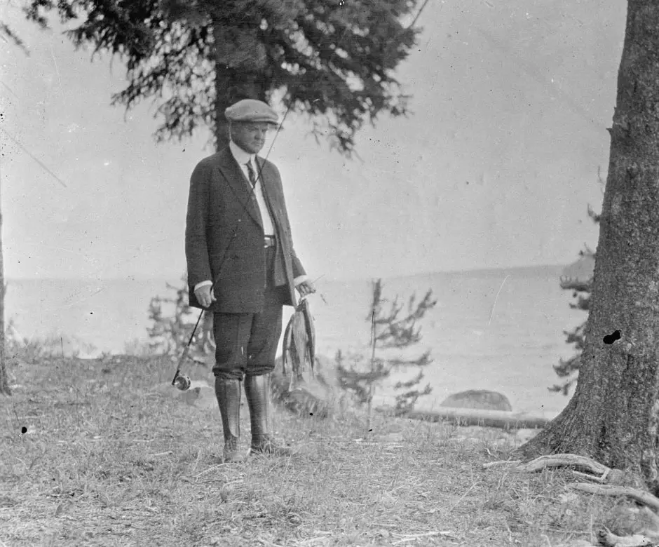 Presidents who love to fish with President Hoover standing on a river bank with fish in hand