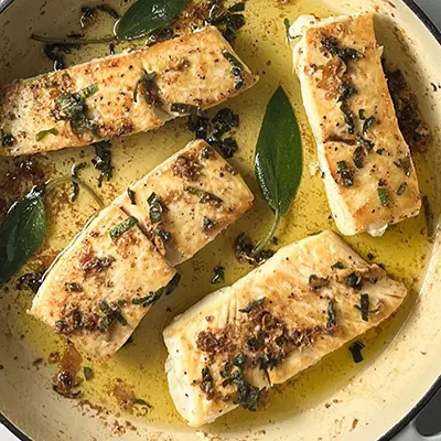 Halibut fillets in a pan with brown butter and sage.