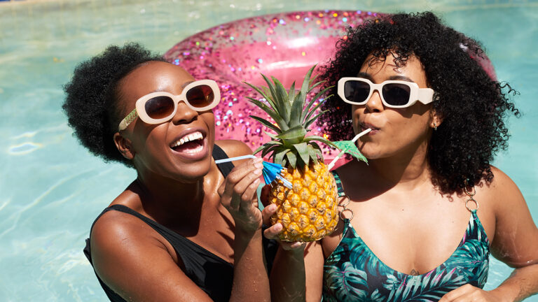Spring break ideas with two women drinking from a pineapple while in a pool.