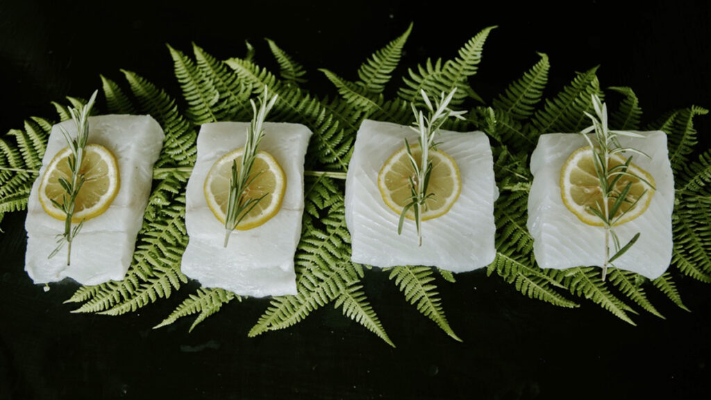 Sliced white fish on ferns topped with rosemary and lemon slices.